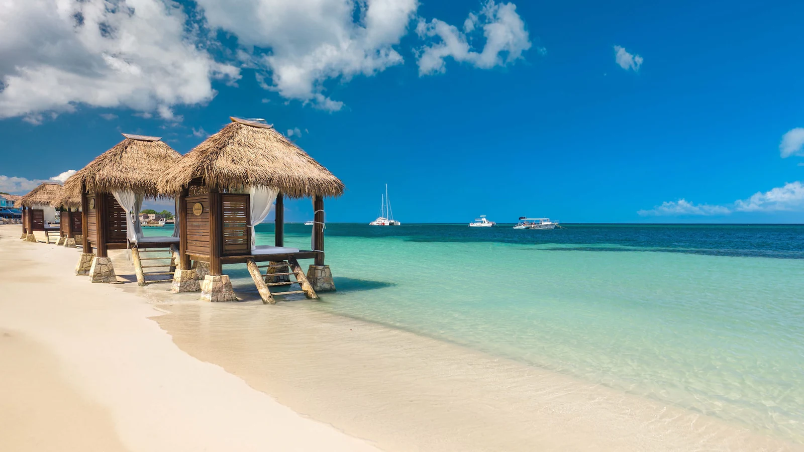 Couple walking hand-in-hand along the private white sand beach at Sandals Montego Bay at sunset