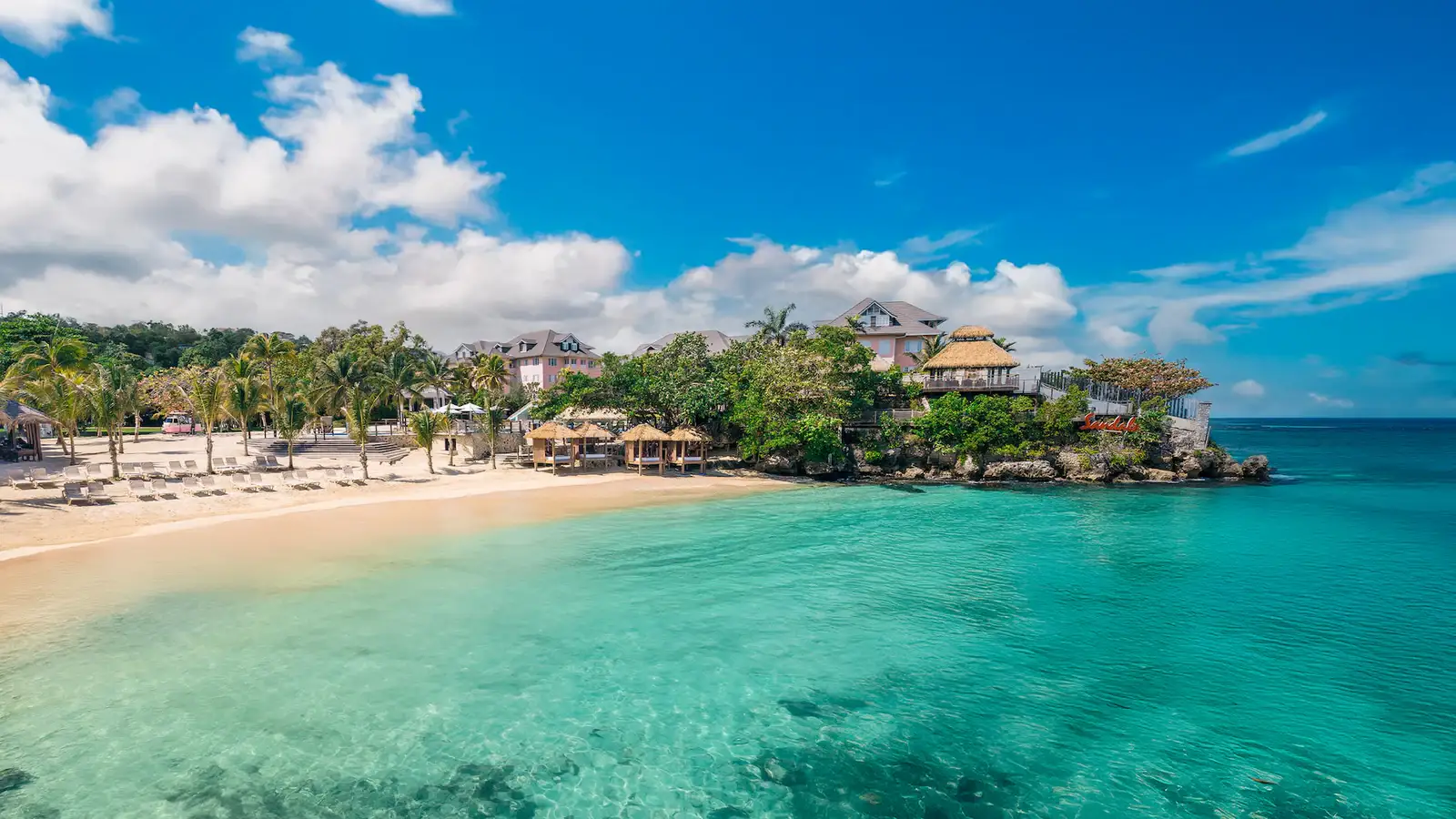 A lively Caribbean beach club at Sandals Ochi with a pier stretching into turquoise water.