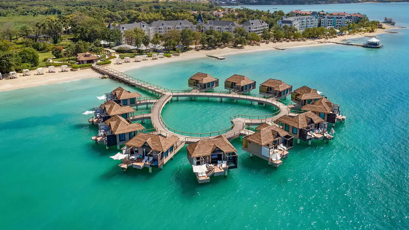 A close up luxurious overwater bungalow at Sandals South Coast at sunset with a couple relaxing.