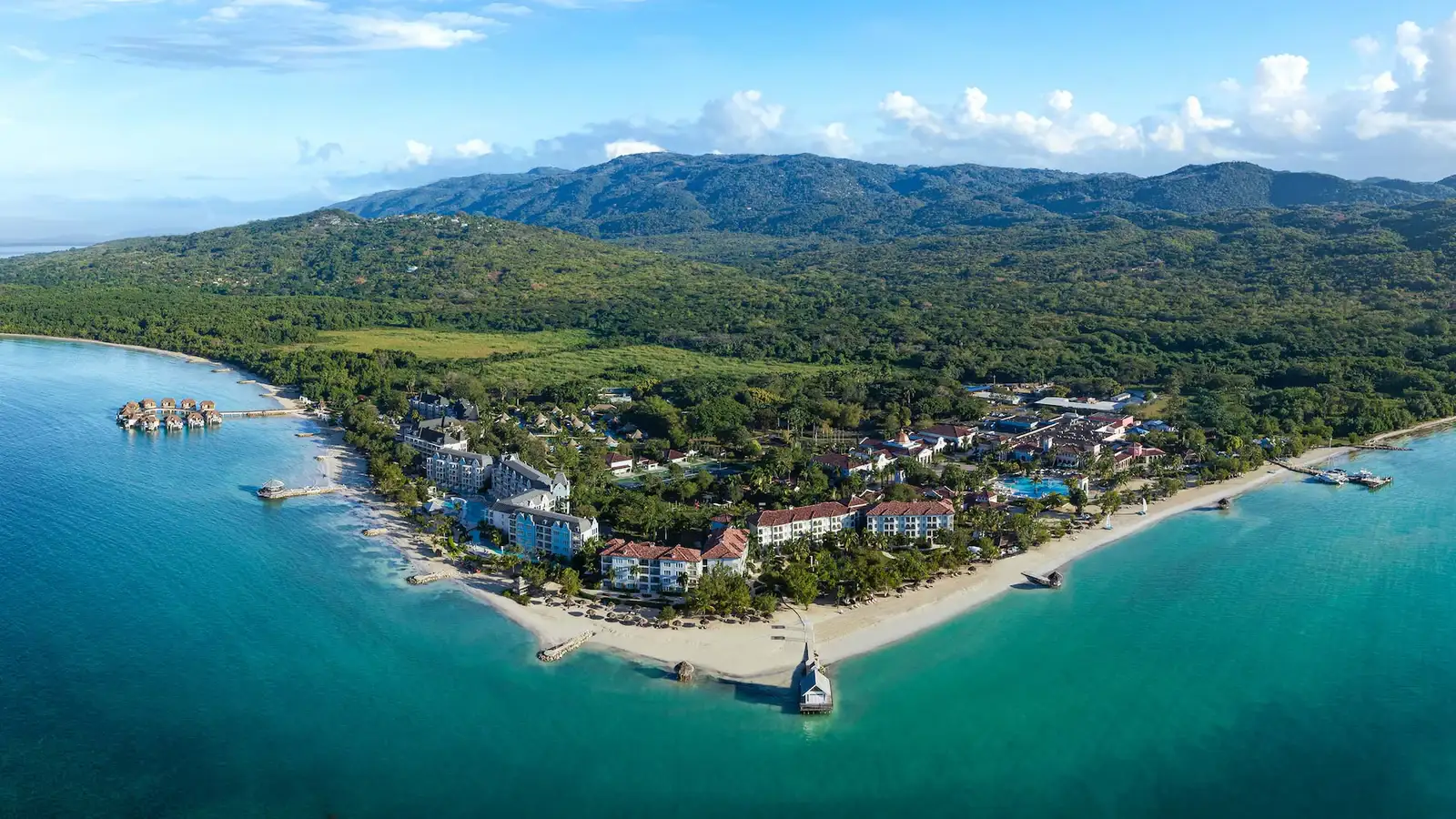 A wide panoramic view of Sandals South Coast, a secluded luxury resort in Jamaica with stunning overwater bungalows arranged in a heart shape.